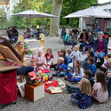 Kinder sitzen in einem Halbkreis vor einer Dame, die etwas vorzeigt. Findet im Schlosshof vom Schloss Landshut statt.
